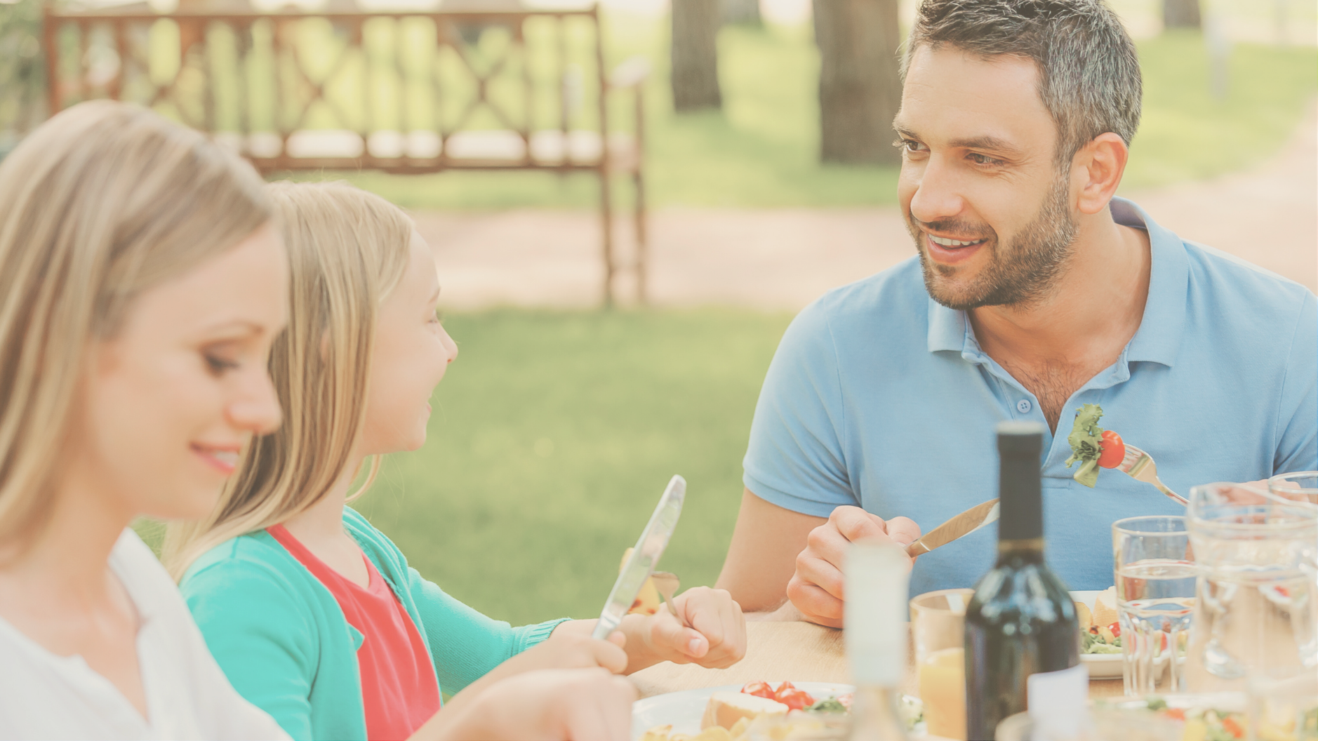A family enjoying dinner al fresco on a picnic table at an RV resort and drinking wine since they enjoy the luxury RV life. 